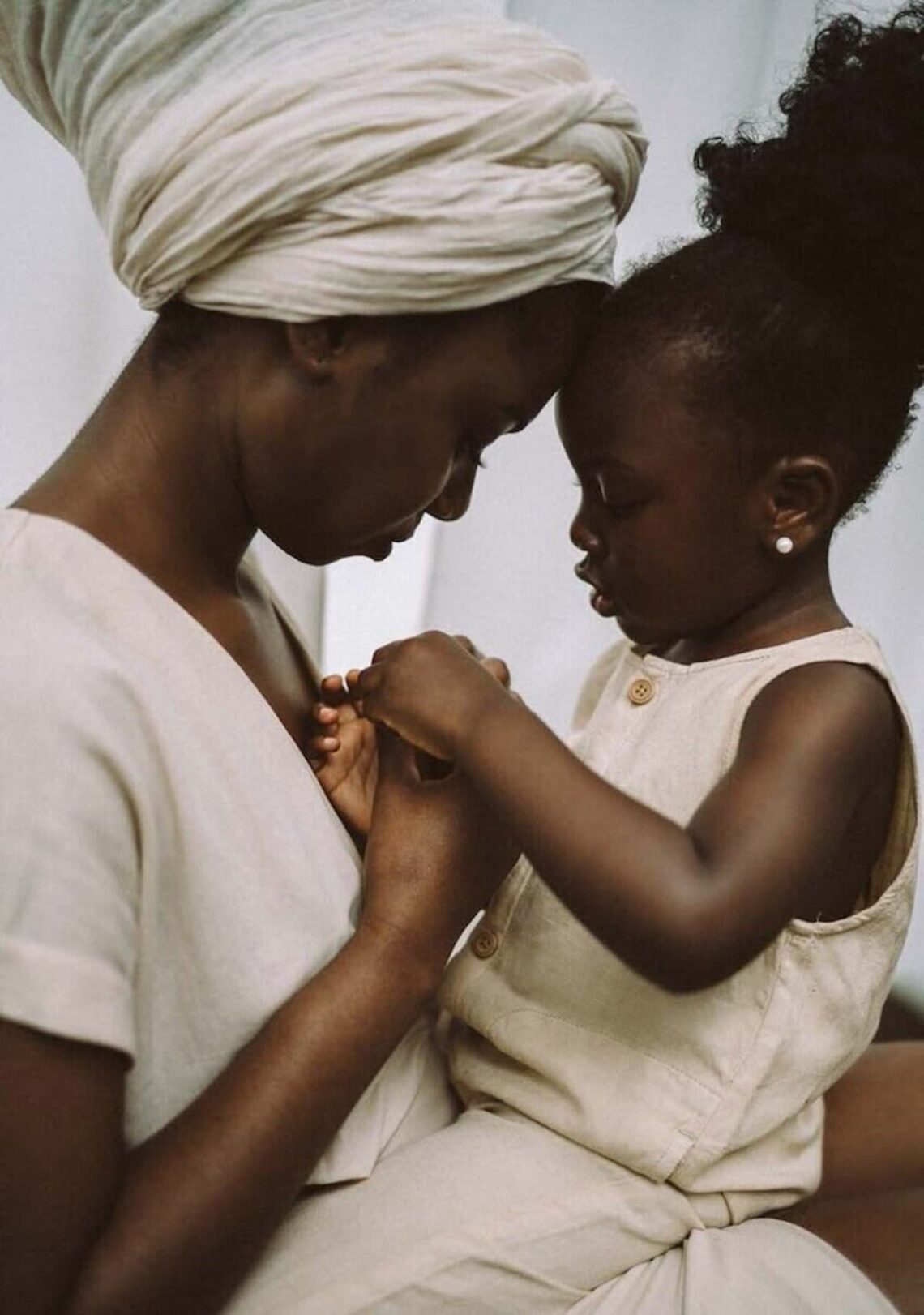 “A young African mother sits closely with her child, their foreheads gently touching as they hold hands — a tender moment of connection and quiet love