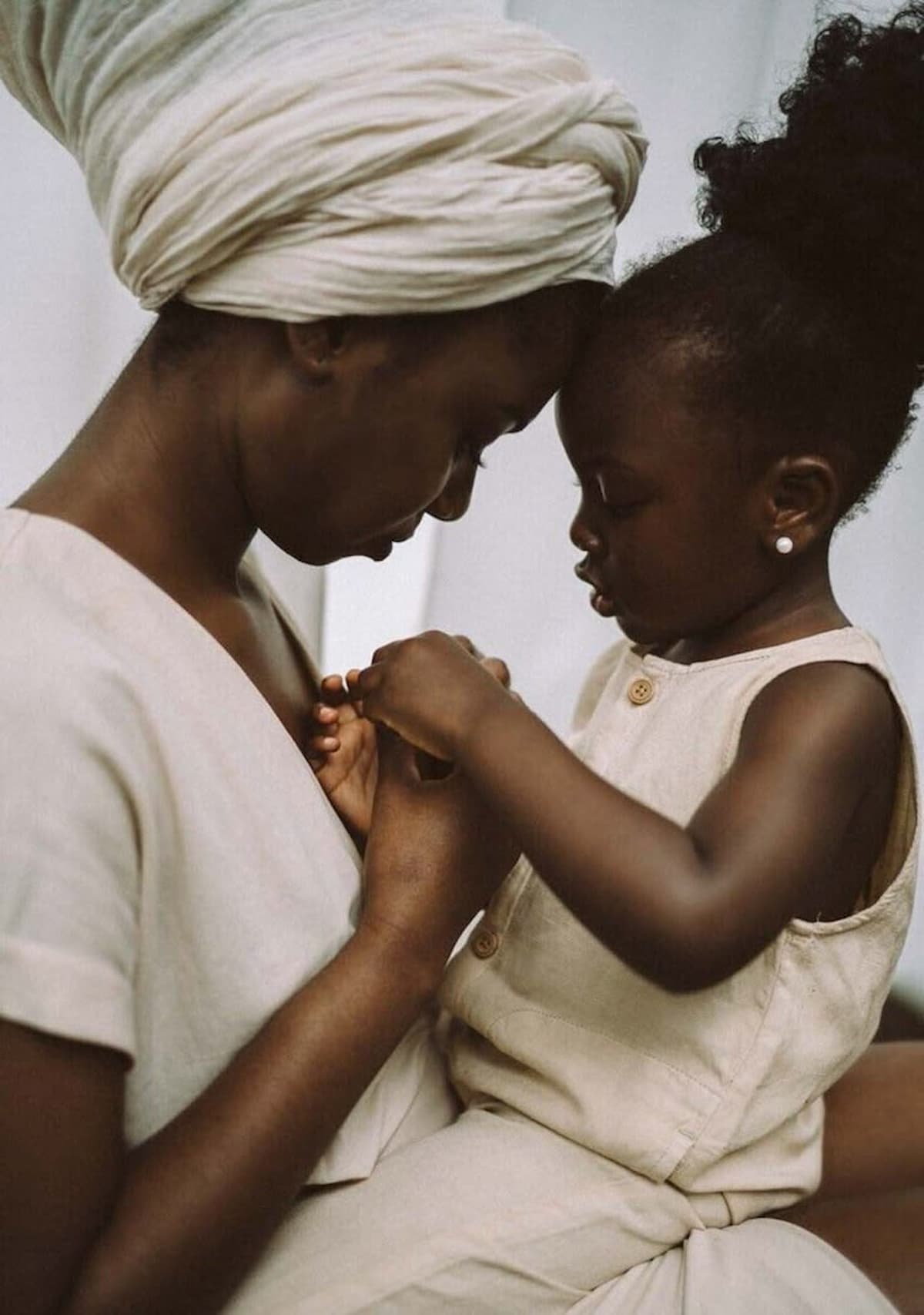 “A young African mother sits closely with her child, their foreheads gently touching as they hold hands — a tender moment of connection and quiet love