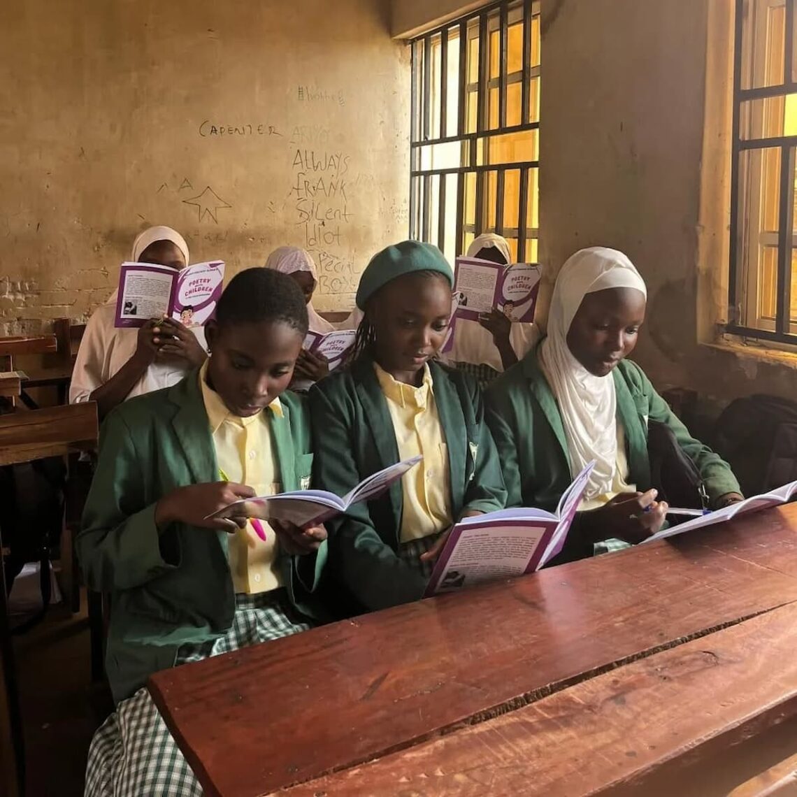 Three school girls in a dimly lit classroom, holding a book titled Poetry Meets Children