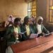 Three school girls in a dimly lit classroom, holding a book titled Poetry Meets Children