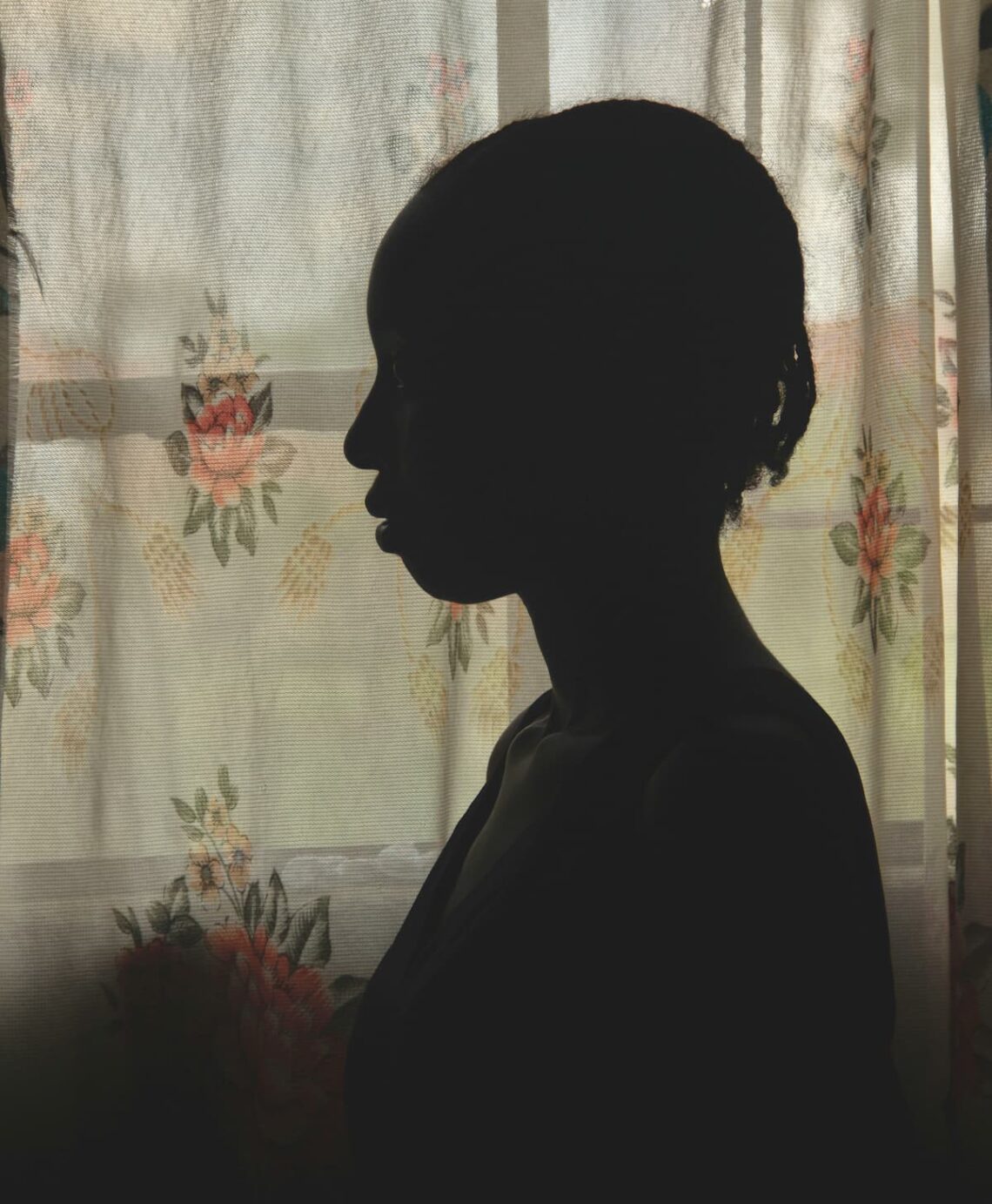 Silhouette of a young girl standing by the widow with the curtains closed.