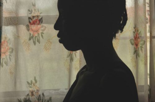 Silhouette of a young girl standing by the widow with the curtains closed.
