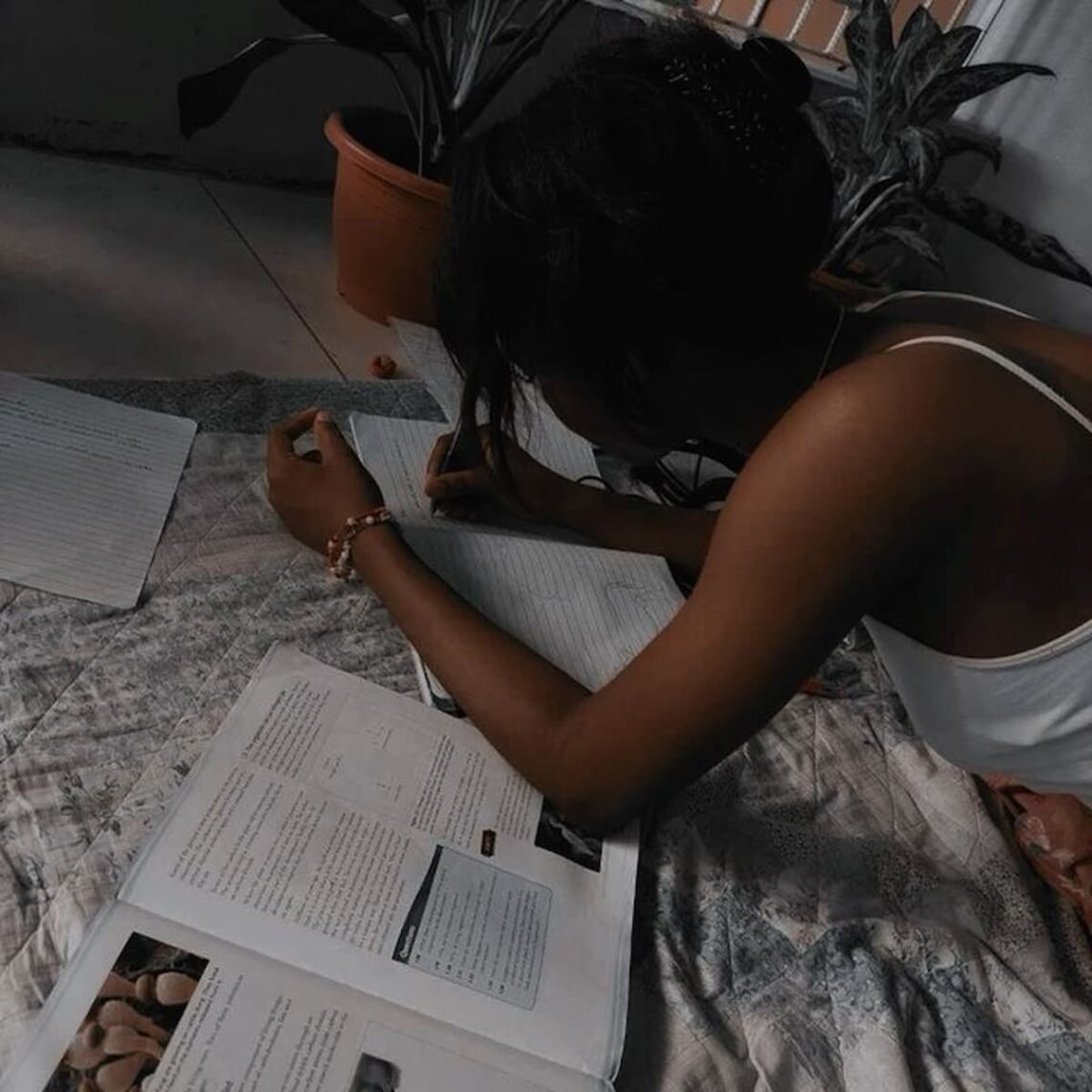 An African girl, lying on a spread cloth on the floor, studying, with books all over the place.