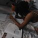 An African girl, lying on a spread cloth on the floor, studying, with books all over the place.