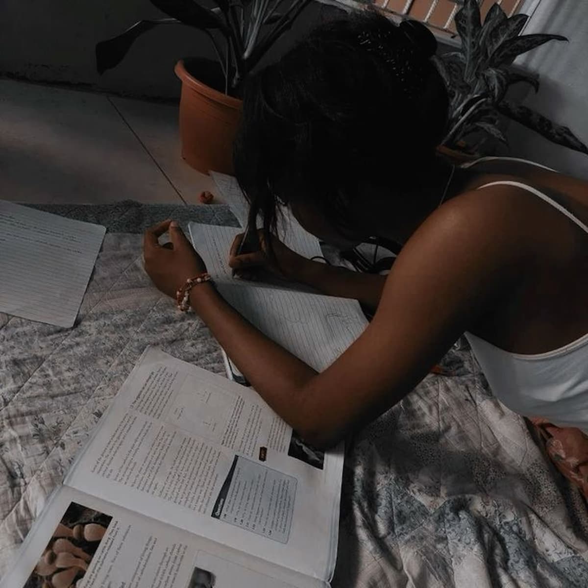 My Nigerian University Story An African girl, lying on a spread cloth on the floor, studying, with books all over the place.