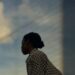 Pensive woman under a soft sky, caught in a moment of emotional clarity.
