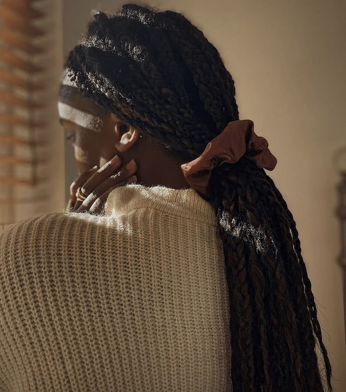 Young woman with long braids tied with a ribbon, looking down in soft warm light.