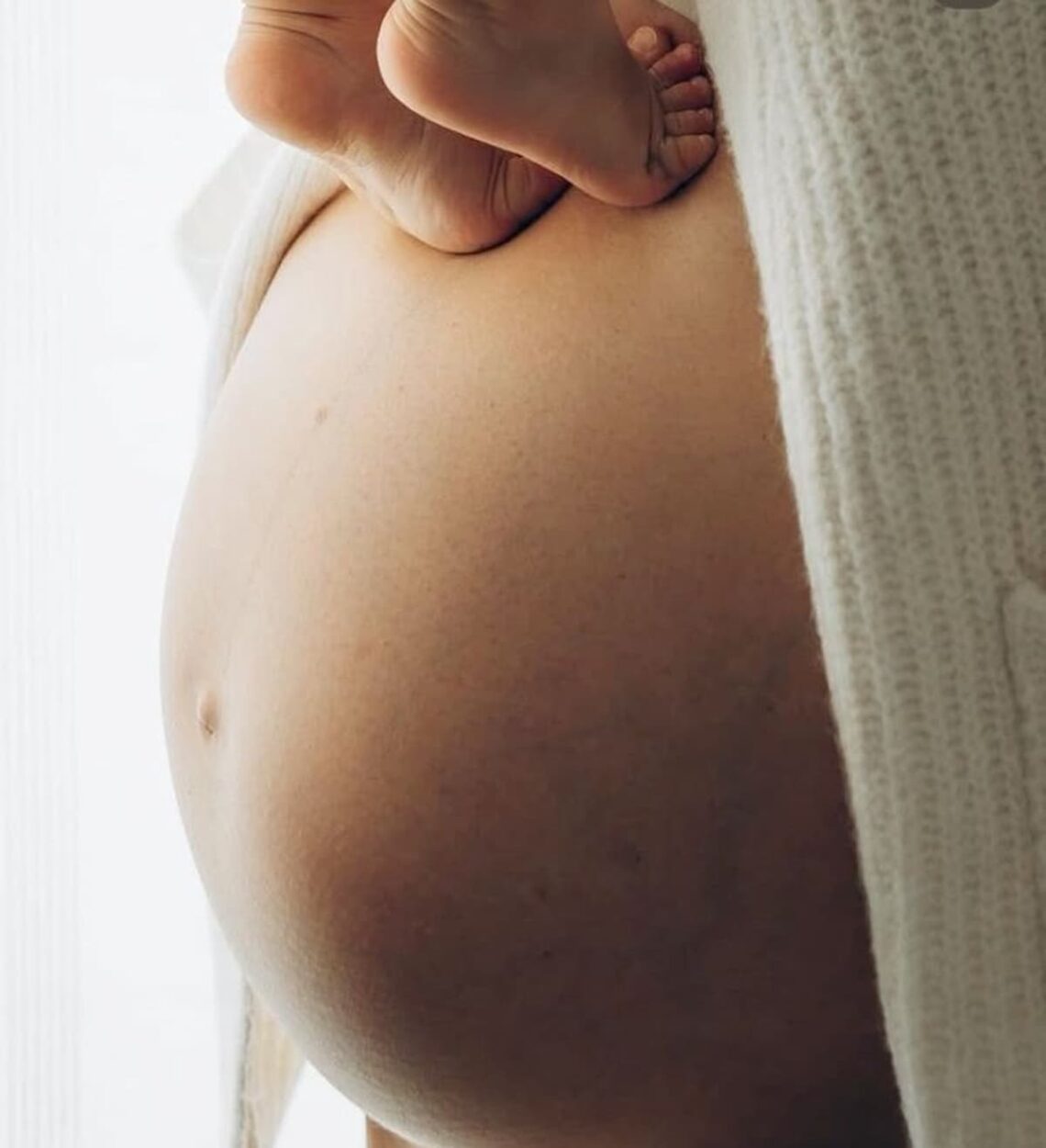 A close shot of a pregnant stomach, with baby feet standing on it.