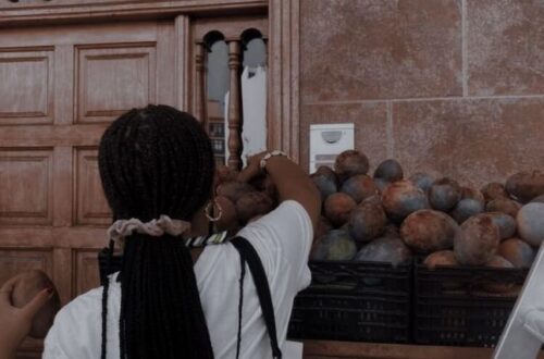 A woman with braids selects fruit from a street market stall.