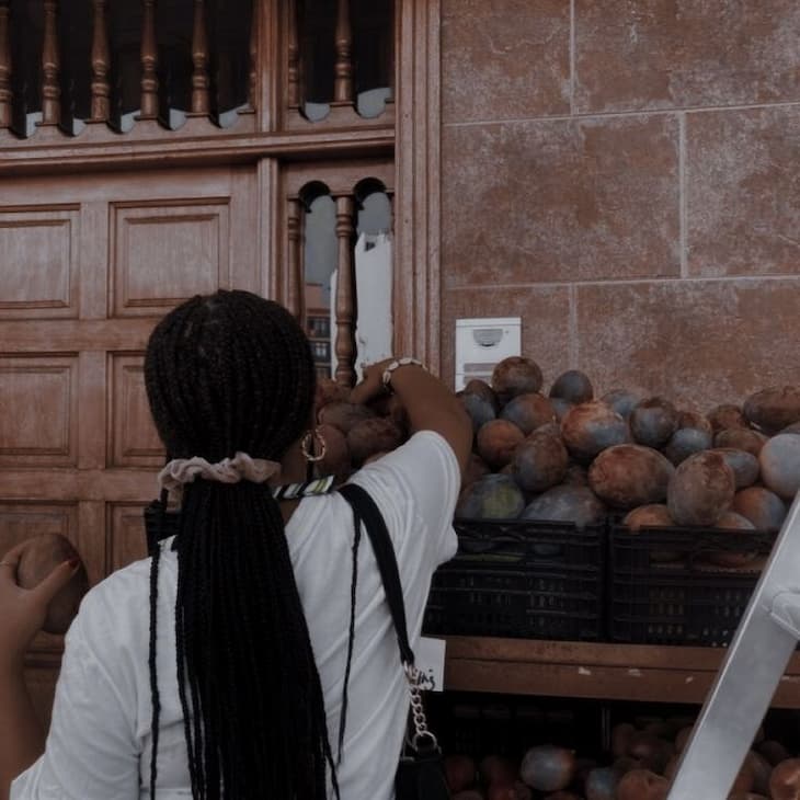 A woman with braids selects fruit from a street market stall.