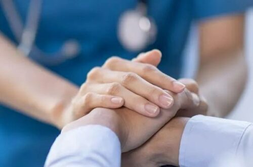 A healthcare worker gently holding a patient’s hand, offering comfort and reassurance in a hospital setting.