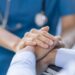 A healthcare worker gently holding a patient’s hand, offering comfort and reassurance in a hospital setting.