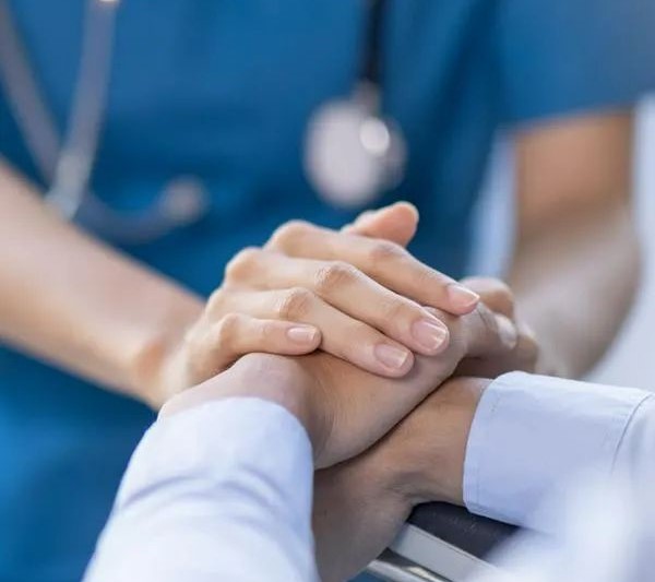 A healthcare worker gently holding a patient’s hand, offering comfort and reassurance in a hospital setting.