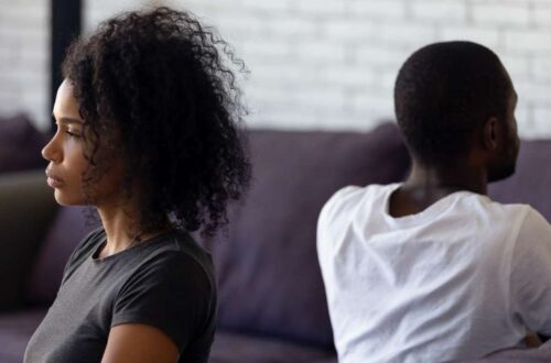 A Black couple backing each other. The lady is wearing a sad look, while the male's face is blurred in the background.