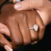 An up-close photo of a female hand wearing a ring. The female hand is holding a man's hand under hers.